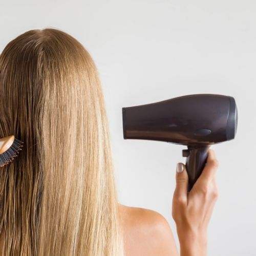 woman blow drying hair with one hand presumably blow drying for lice