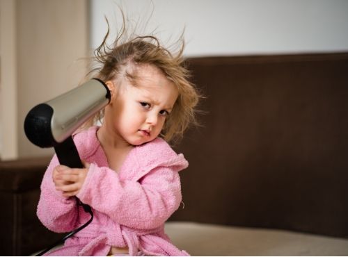 small child blow-drying her hair, presumably blow-drying for head lice