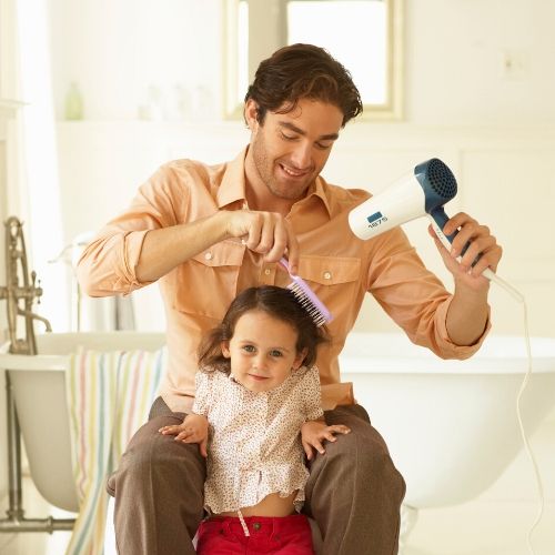 father blow-drying his daughters hair, presumably blow-drying for head lice