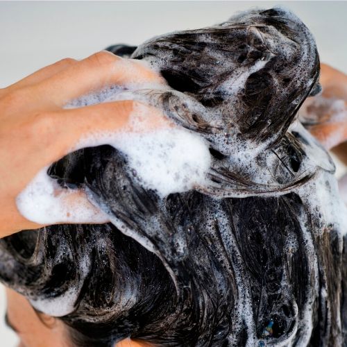 woman washing her hair, presumably with tea tree oil shampoo for head lice