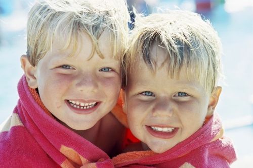 Two young children sharing a towel after swimming, presumably spreading head lice