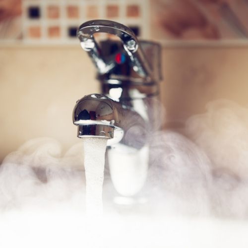 A faucet releasing hot water, steam is rising from the sink.