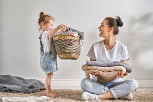 A young girl carries a load of laundry to her mother who is folding towels.