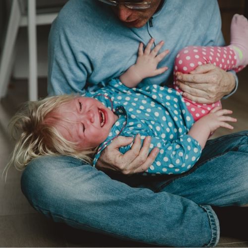 A crying child in her parent's arms.