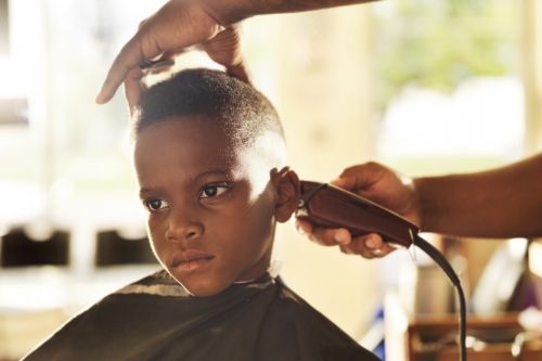 dark skinned boy getting his head shaved, presumably for head lice