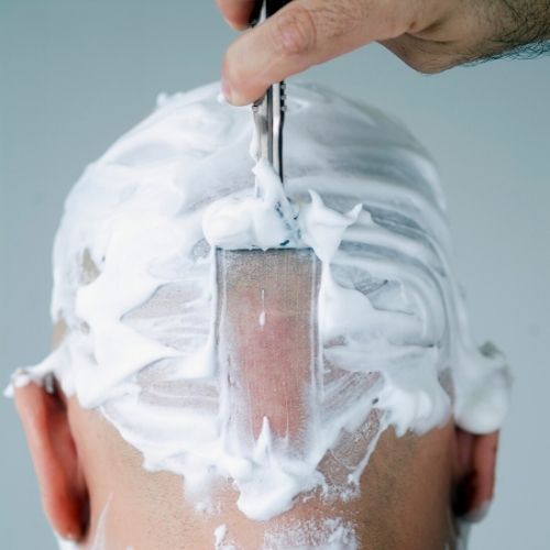 man shaving his head with razor and shaving cream, presumably for head lice
