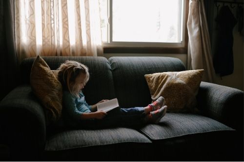 A girl with head lice sitting on a couch reading a book