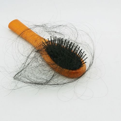 A hair brush with a wooden handle and black bristles. There is black hair in the brush.