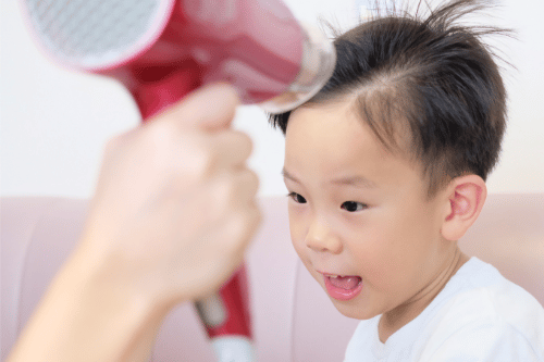 mother blow-drying child's hair, presumably child has head lice