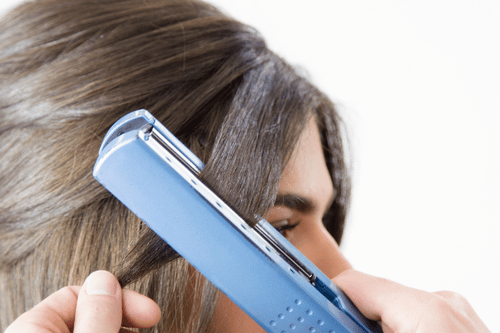 brunette flat ironing hair with blue flat iron, presumably flat ironing for lice