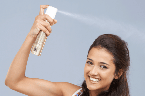 woman spraying lice spray into her hair